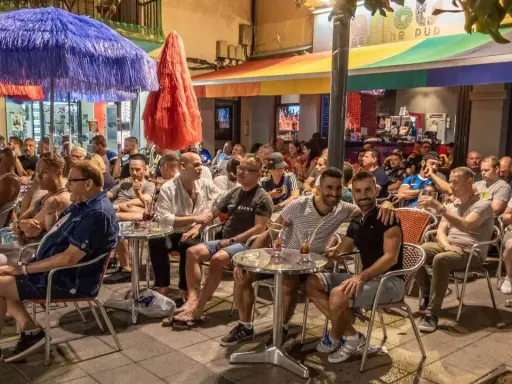 People enjoying drinks at outdoor tables outside gay bars in Sitges, Spain.