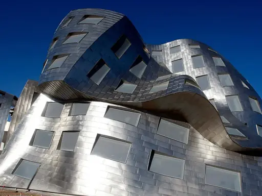 Edificio dalle forme ondulate e metalliche, una delle opere di Frank Gehry, con finestre quadrate e rettangolari.