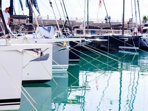 Plusieurs bateaux de plaisance sont amarrés dans un port. La coque du bateau, blanche et grise, est visible au premier plan, avec une ancre argentée.