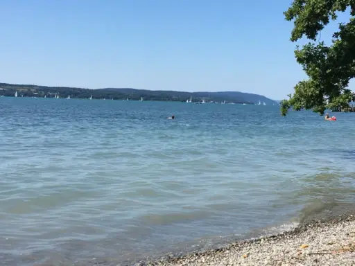 Sonniger Bodensee-Strand, ein echter Geheimtipp. Segelboote gleiten über das Wasser, während ein paar Schwimmer die Ruhe genießen.