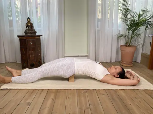 Kvinna i yin yoga-position med en kudde under ryggen. Denna lugna praktik kan stödja din resa mot viktminskning.