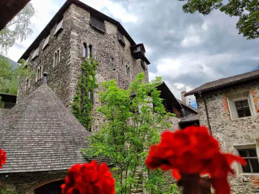 Il castello di Campo Tures, con le sue mura in pietra e il tetto a scandole, si erge maestoso tra il verde e fiori rossi.