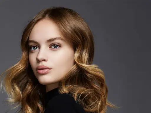 Porträt einer jungen Frau mit welligem, braunem Haar, das mit Balayage-Technik aufgehellt wurde.