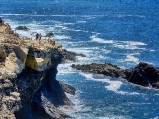Acantilados rocosos y el mar azul cerca de las cuevas de Ajuy. Turistas observan el paisaje desde un mirador.