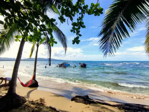 Sonniger Strand in Puerto Viejo mit Palmen, Hängematte und Menschen im türkisfarbenen Meer.