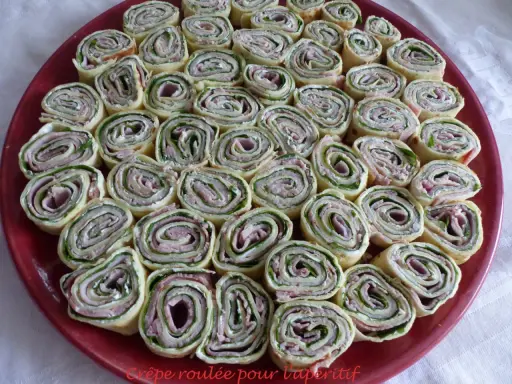 Une assiette rouge remplie de délicieuses crêpes roulées apéritif, garnies de jambon, fromage frais et herbes. Parfait pour un apéritif convivial.