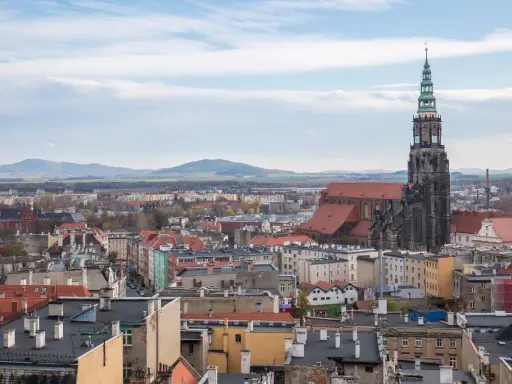 Widok na świdnica rynek z dominującą wieżą katedry i dachami kamienic. W tle góry.