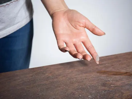 Mano con polvo en los dedos sobre una mesa de madera, mostrando porque sale tanta pelusa en casa.
