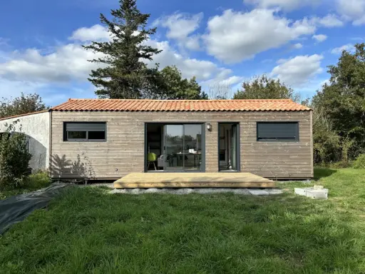 Une petite maison en bois avec une terrasse, idéale pour un plan maison 5m sur 10m. Le toit est couvert de tuiles rouges.
