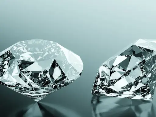 Due diamanti scintillanti, uno rotondo e uno a goccia, riflettono la luce. Uno dei due, un diamante brown, brilla con sfaccettature perfette.