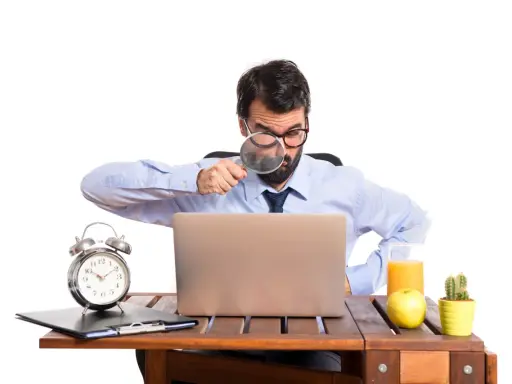 Mężczyzna z lupą bada laptopa, szukając odpowiedzi, czy skstore jest legit. Na biurku budzik, jabłko i sok.