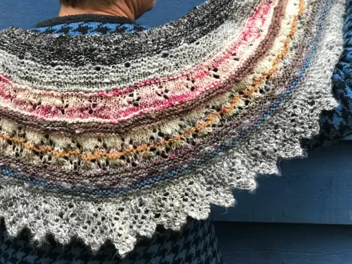 Un chal de lana tejido con hilos de colores, con un intrincado diseño de encaje y bordes festoneados. Los mantoncillos de crochet son una obra de arte.