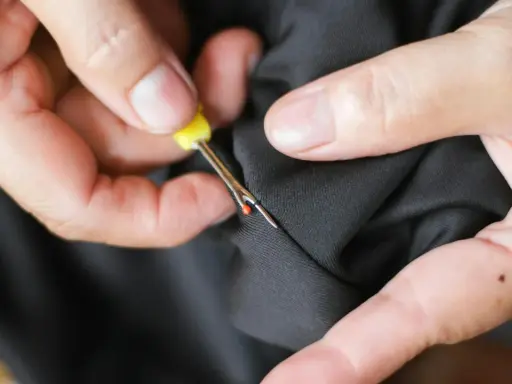 Hands use a seam ripper to open a pocket on black fabric. This is how suit pockets are sewn shut to maintain their shape during shipping.