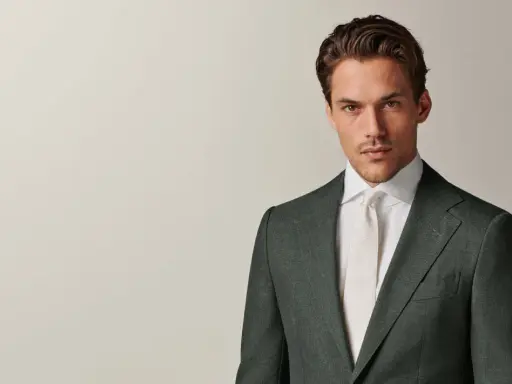 A man in a dark green suit and white shirt with a cream tie. This timeless look embodies the perennial suit meaning of enduring style and sophistication.
