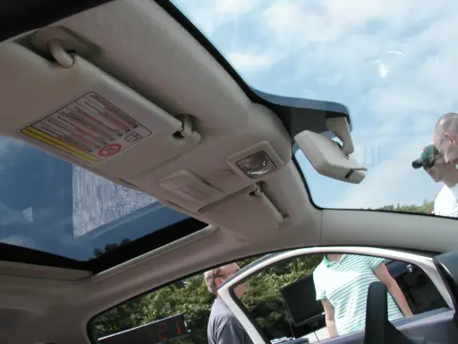 Interior de un Fiat 500 con el techo solar abierto, mostrando el parasol y el espejo retrovisor.