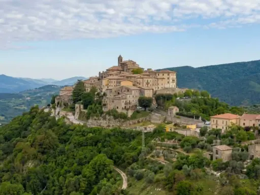 Borgo medievale su una collina verde, uno dei tanti **paesi da vedere vicino Roma**, con case in pietra e un campanile.