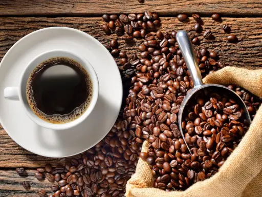 Eine Tasse heißer Kaffee neben einer Schaufel voller gerösteter Bohnen und einem Jutesack. Der Duft von perfekt gebrühtem Filterkaffee liegt in der Luft.