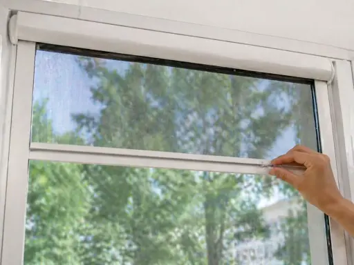 Main tenant ajuste sa moustiquaire de fenêtre pour profiter de l'air frais sans insectes.