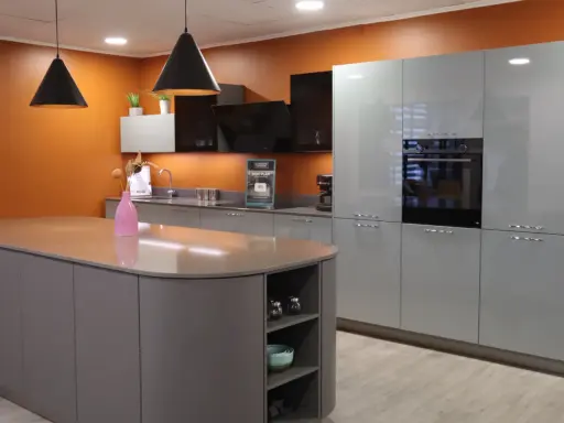 Cuisine moderne avec îlot central et armoires grises. Les murs orange vif contrastent avec les surfaces épurées, créant une ambiance chaleureuse. Une cuisine sans hotte, mais avec un design élégant.