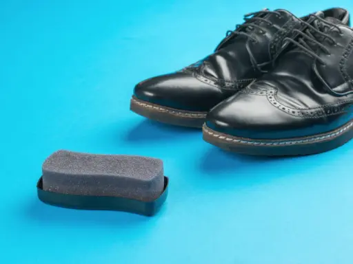 Czarne buty ze sztucznej skóry i gąbka do pastowania. Czy można pastować buty ze sztucznej skóry? Tak, specjalnymi preparatami.