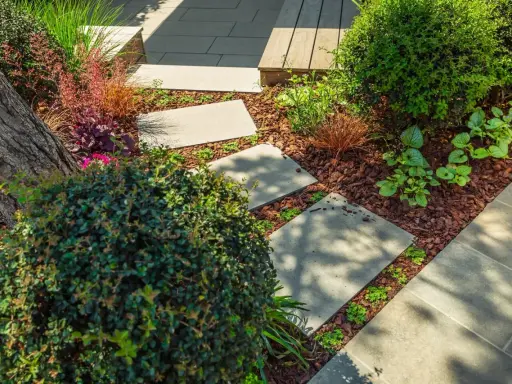 Schritt für Schritt: Gehwegplatten verlegen in einem üppigen Garten mit Rindenmulch und verschiedenen Pflanzen.