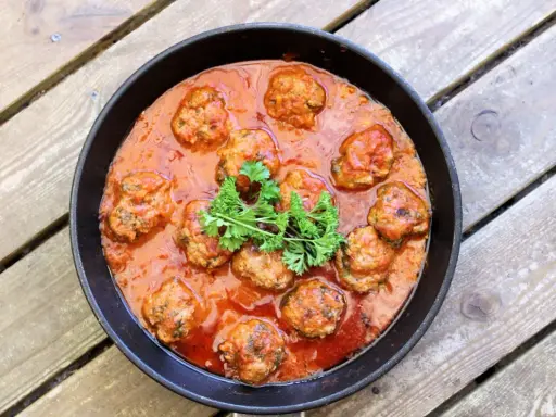 Frikadeller i tomatsås, en klassisk svensk rätt, serveras i en gjutjärnspanna. Garnerad med persilja.