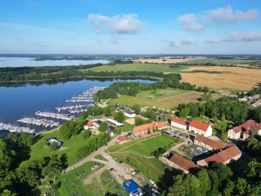 Malowniczy widok na jezioro z przystanią pełną żaglówek, idealne miejsce na długi weekend czerwcowy. W oddali pola i zabudowania.