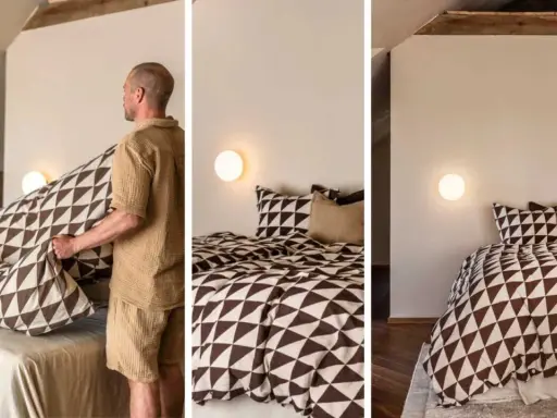 Gustav Ovland bäddar en säng med ett mönstrat påslakan. Sängen är bäddad med kuddar och ett täcke med geometriskt mönster.