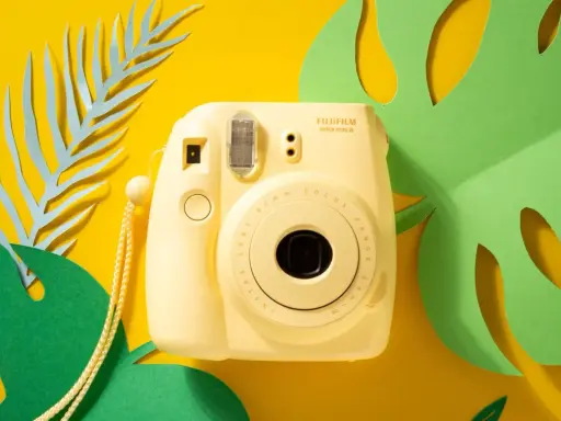 Żółty aparat natychmiastowy Fujifilm Instax mini 8 na tle tropikalnych liści.