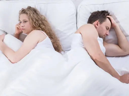 Para, odwróceni do siebie plecami w łóżku, zmartwiona kobieta i mężczyzna z ręką na czole. Czy to pochwica? Co to za problem?