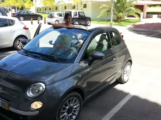 Frau lehnt sich aus einem grauen Fiat 500 Cabrio, bereit für eine Spritztour. Hier sind einige mietwagen portugal tipps für Ihren Urlaub!