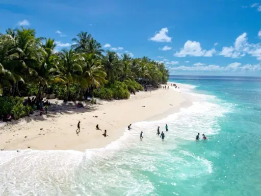 Spiaggia tropicale con palme e persone che nuotano nell'acqua cristallina dell'atollo di Maafushi.