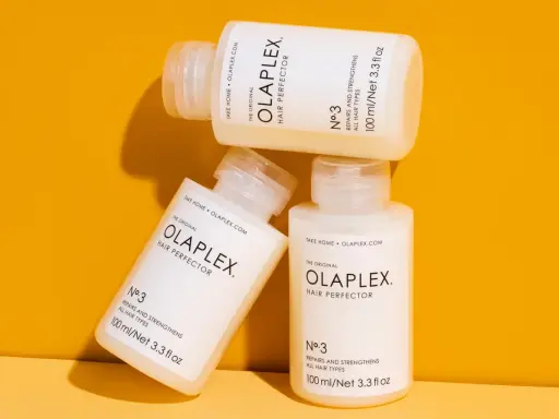 Drei Flaschen der OLAPLEX Serie, "Hair Perfector No.3", liegen übereinander auf einem orangen Hintergrund.