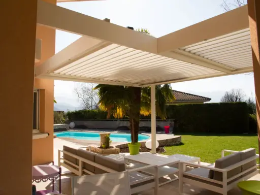 Une pergola bioclimatique moderne avec des lames orientables protège un salon extérieur et une piscine.