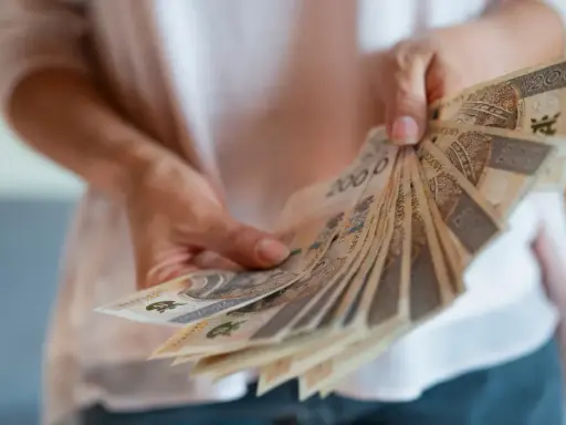 Dłonie trzymają wachlarz polskich banknotów. Zastanawiasz się, czy nagroda jubileuszowa wlicza się do emerytury?