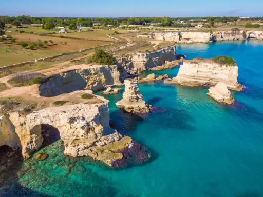 Scogliere bianche e mare turchese in una splendida **Puglia estate**. Faraglioni emergono dall'acqua cristallina, un vero paradiso.