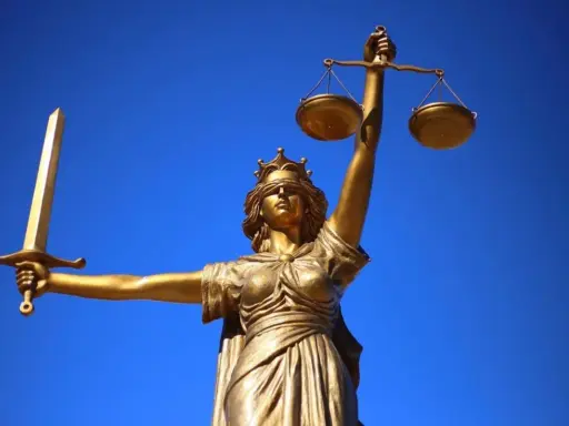 Statua dorata della Giustizia con spada e bilancia, simbolo dei giudici ordinari, contro un cielo blu intenso.