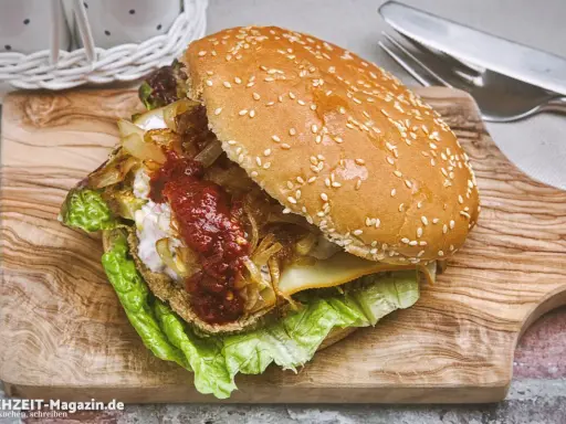 Ein saftiger vegetarischer Burger mit Salat, karamellisierten Zwiebeln und scharfer Sauce auf einem Holzbrett.