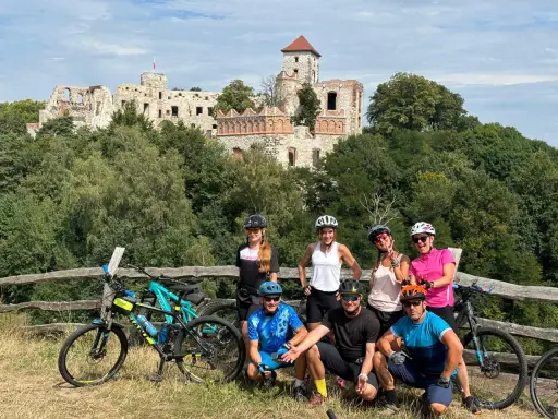 Grupa rowerzystów na tle ruin zamku. Planują noclegi na Szlaku Orlich Gniazd rowerem.