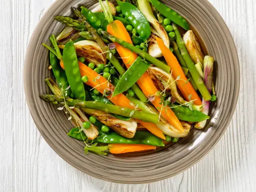 Jardinière de légumes colorée : carottes, pois, asperges et fenouil grillés, garnie de thym frais. Un plat sain et appétissant.
