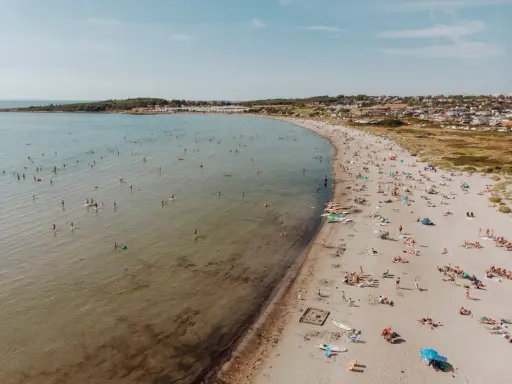En livlig strand i Halland med många badande och solande människor. Vattnet är klart och inbjuder till lek.