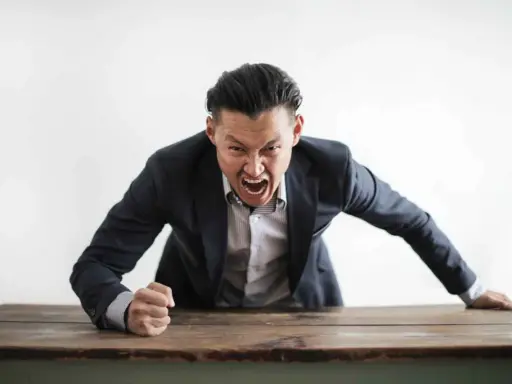 Wütender Mann im Anzug schreit über einen Tisch. Darf ein Lehrer Schüler anschreien?