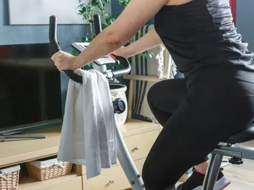 Kobieta w czarnym stroju ćwiczy na rowerze stacjonarnym, spędzając godzinę jazdy na rowerze stacjonarnym w domowym zaciszu.