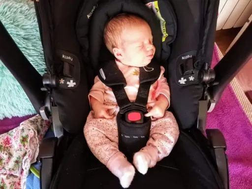 Śpiący noworodek w różowym pajacyku z króliczkami w foteliku Kiddy. Wkładka noworodkowa zapewnia komfort i bezpieczeństwo.