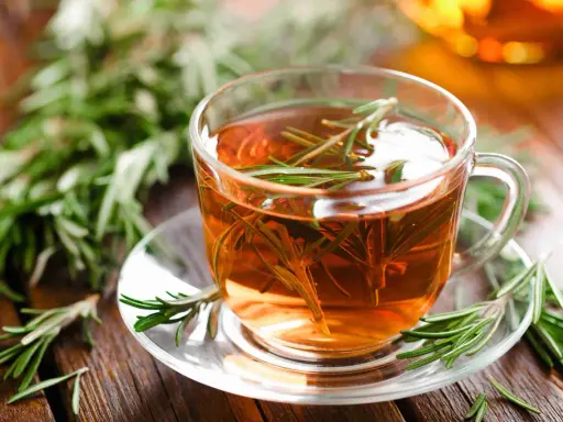 Une tasse de tisane romarin, avec des brins de romarin frais sur la soucoupe et en arrière-plan.