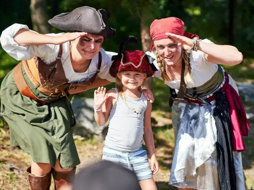 Två pirater och ett barn ler och hälsar. En rolig dag med aktiviteter för barn.