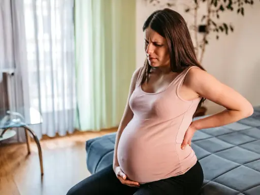 Schwangere Frau im 3. Trimester mit oberbauchschmerzen, hält sich den Rücken.