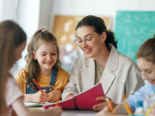 Lehrerin erklärt Kindern etwas aus einem Buch. Eine Tafel mit Rechenaufgaben im Hintergrund deutet auf die Bedeutung von Bildungspolitik für die Zukunft hin.