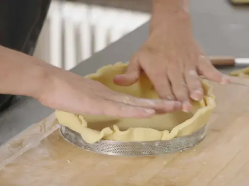 Mains expertes pour foncer une pâte dans un cercle à tarte. La pâte est étalée et ajustée sur les bords.