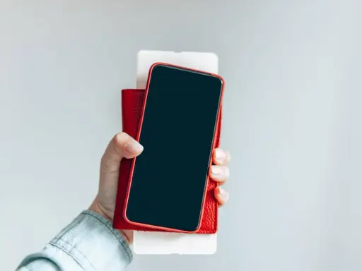 Dłoń trzyma iPhone'a w czerwonym etui. Czy iPhone jest bezpieczny? Zależy od użytkownika i jego nawyków.